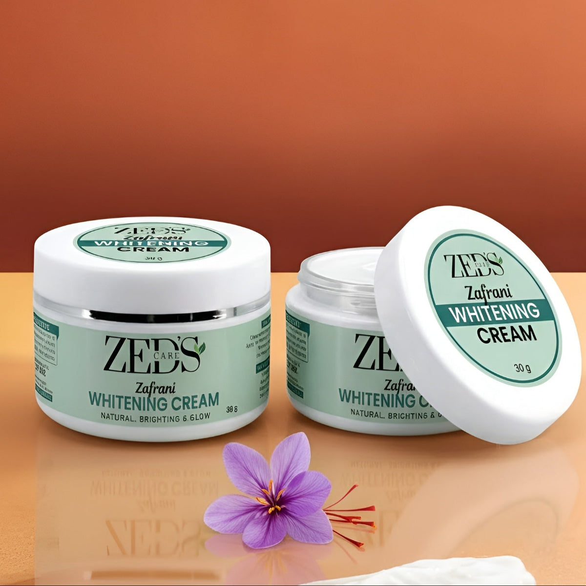 Two jars of Zeds care Zafarni Whitening Cream on a reflective surface with a purple flower.